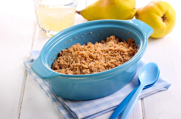 Un crumble de poire dans un plat bleu avec des poires derrière